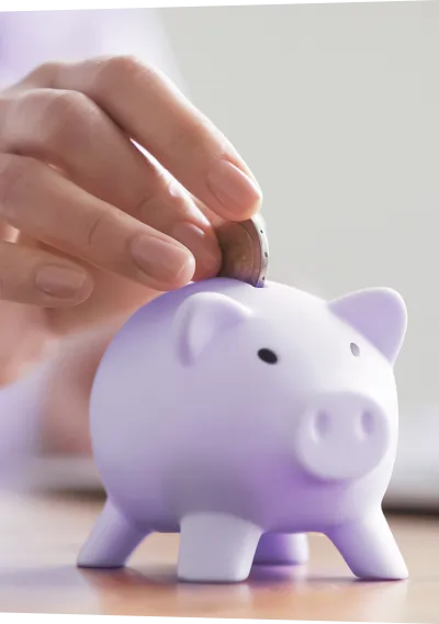 Mão inserindo moeda em porquinho lilás.